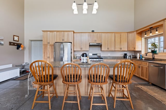 kitchen featuring light brown cabinetry, under cabinet range hood, a sink, appliances with stainless steel finishes, and a towering ceiling