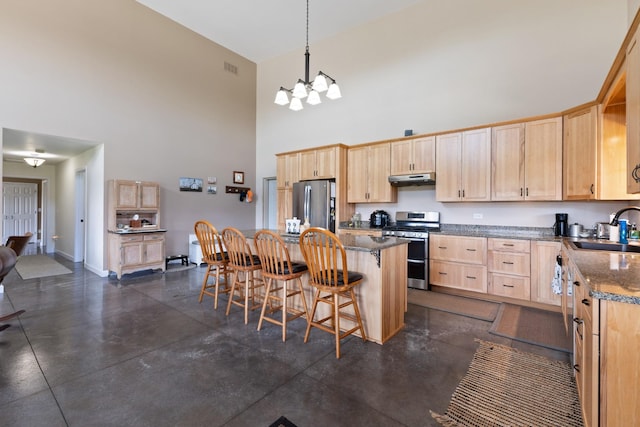 kitchen with light brown cabinets, under cabinet range hood, a towering ceiling, stainless steel appliances, and a sink