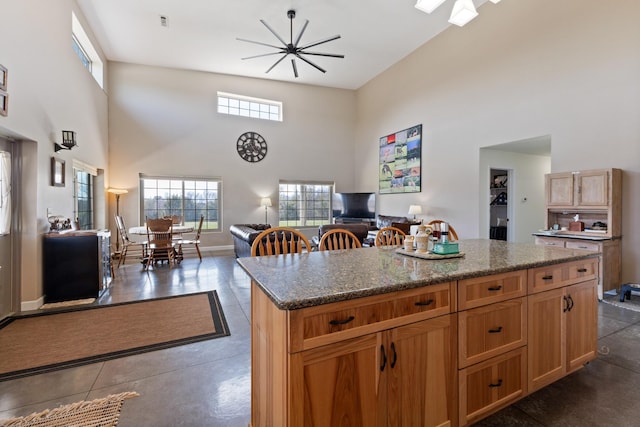 kitchen featuring a kitchen island, finished concrete floors, open floor plan, dark stone counters, and a towering ceiling
