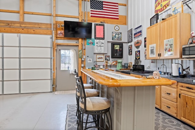 kitchen featuring dark countertops, a breakfast bar, a sink, finished concrete floors, and stainless steel microwave