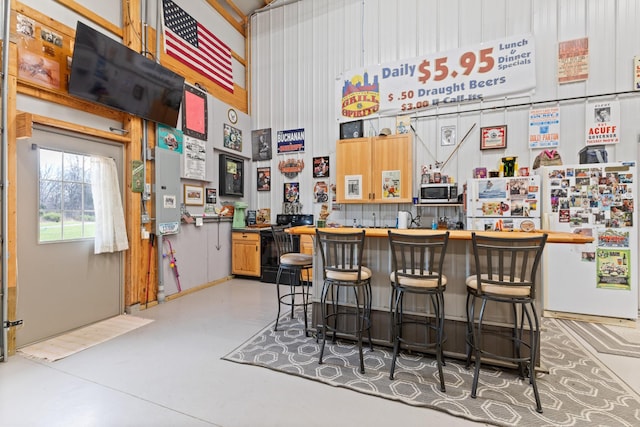 bar featuring stainless steel microwave, concrete flooring, bar, freestanding refrigerator, and a high ceiling