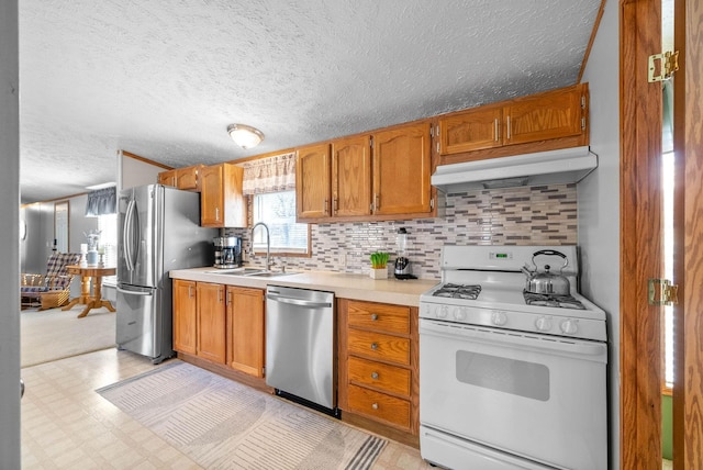 kitchen with light floors, a sink, stainless steel appliances, light countertops, and under cabinet range hood