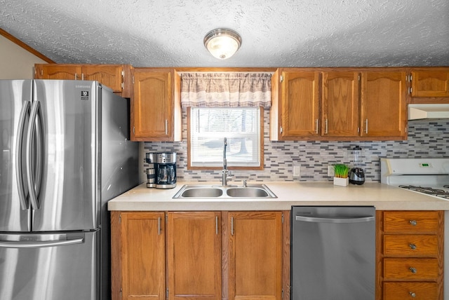 kitchen with under cabinet range hood, light countertops, brown cabinets, appliances with stainless steel finishes, and a sink