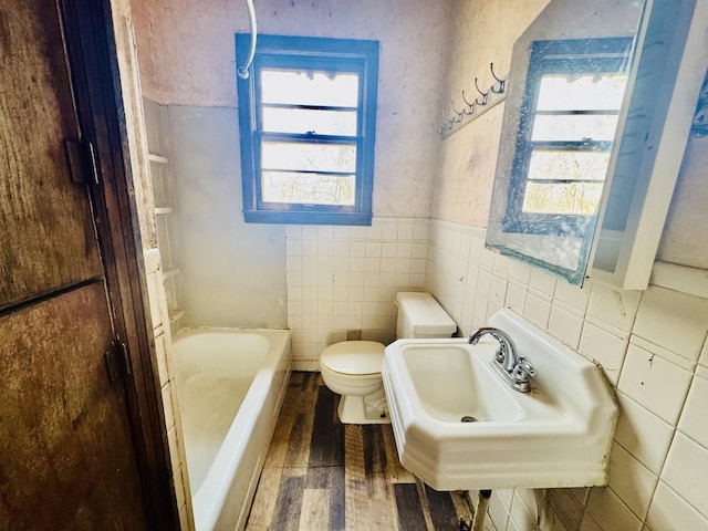 bathroom featuring wood finished floors, a wainscoted wall, tile walls, toilet, and a washtub