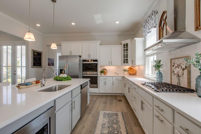 kitchen with a sink, ornamental molding, light countertops, stainless steel appliances, and wall chimney range hood