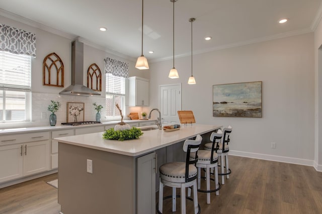 kitchen featuring a sink, wood finished floors, wall chimney exhaust hood, crown molding, and stainless steel gas cooktop