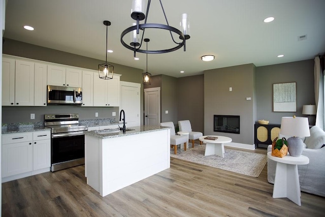 kitchen with light stone counters, wood finished floors, a sink, stainless steel appliances, and a large fireplace