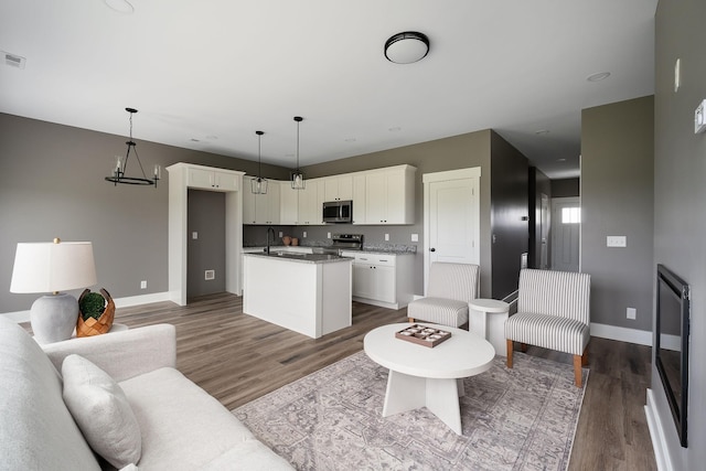 living room featuring an inviting chandelier, visible vents, wood finished floors, and baseboards