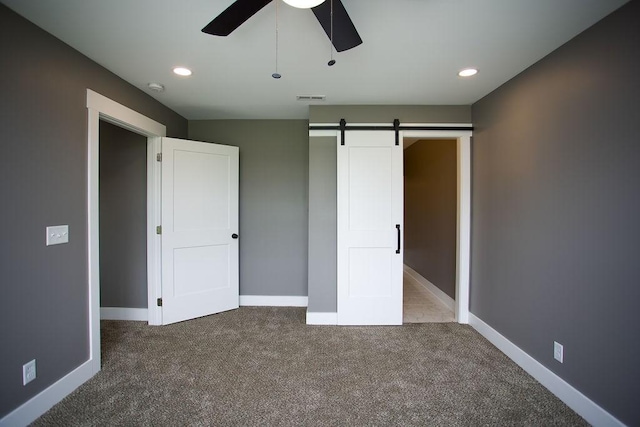 unfurnished bedroom featuring visible vents, baseboards, a barn door, and carpet floors