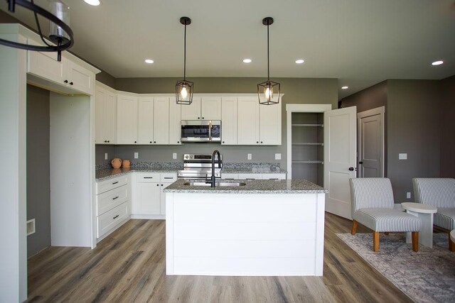 kitchen with a sink, light stone countertops, appliances with stainless steel finishes, and wood finished floors