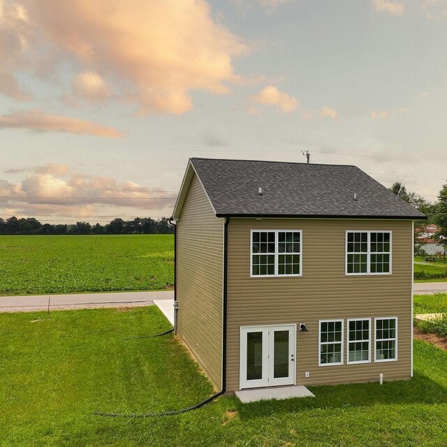 back of house at dusk featuring a lawn and roof with shingles