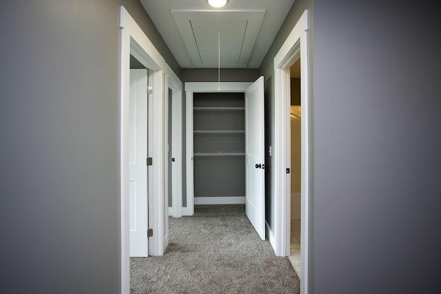 corridor with baseboards, light carpet, and attic access