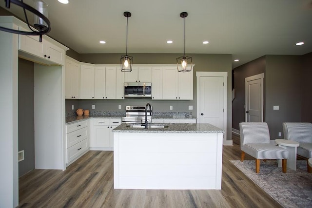 kitchen with dark wood-style floors, light stone countertops, stainless steel appliances, and a sink