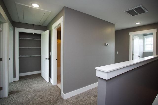 hall with light carpet, visible vents, attic access, and baseboards