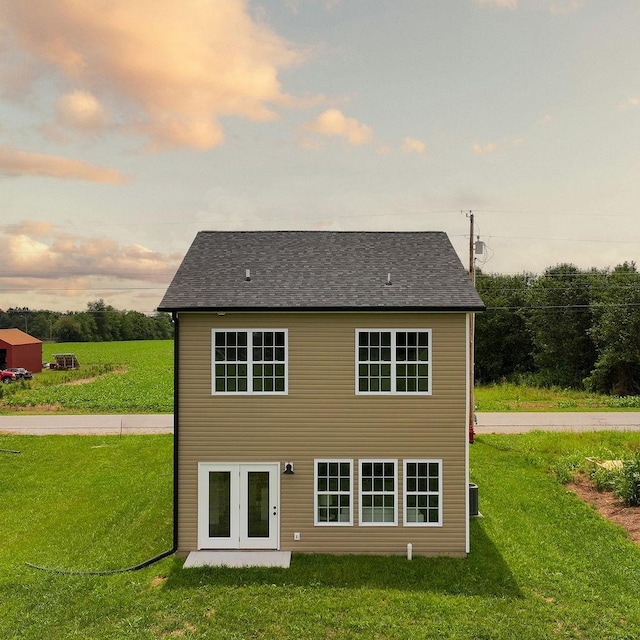 back of property at dusk with a yard, central AC unit, and a shingled roof