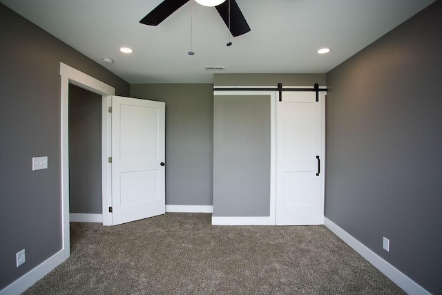 unfurnished bedroom with visible vents, dark carpet, recessed lighting, a barn door, and baseboards