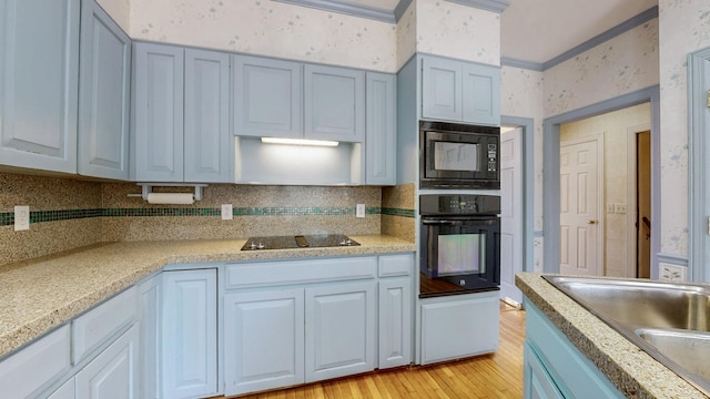 kitchen featuring light wood finished floors, black appliances, wallpapered walls, crown molding, and light countertops