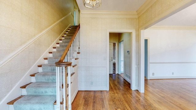 staircase with wood finished floors, baseboards, visible vents, ornamental molding, and a chandelier