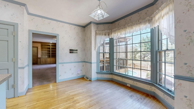 unfurnished dining area with ornamental molding, wallpapered walls, and wood-type flooring