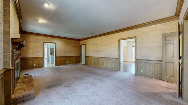 unfurnished room with a brick fireplace, carpet flooring, and wainscoting