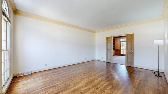 empty room with visible vents, baseboards, wood finished floors, and ornamental molding