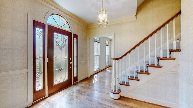 foyer with stairway, a notable chandelier, wood finished floors, and ornamental molding