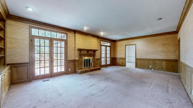 unfurnished living room with a fireplace, french doors, a wainscoted wall, and light colored carpet