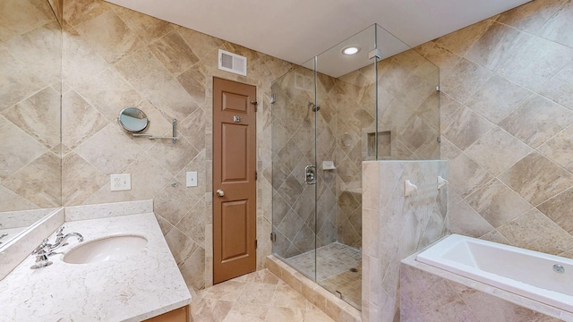 bathroom with visible vents, a garden tub, a stall shower, tile walls, and vanity