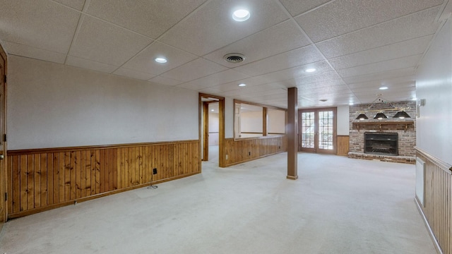 unfurnished living room with visible vents, a brick fireplace, wood walls, carpet flooring, and wainscoting