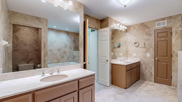 full bathroom with tile walls, two vanities, visible vents, and a sink