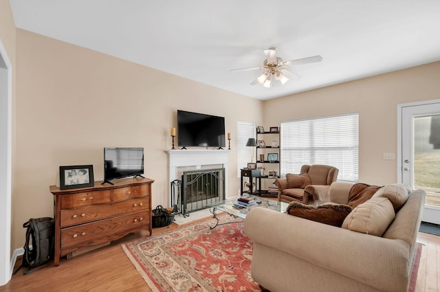 living room with a fireplace with raised hearth, light wood-style flooring, and a ceiling fan