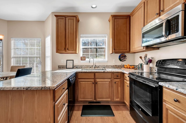 kitchen featuring light wood-type flooring, light stone counters, a peninsula, black appliances, and a sink