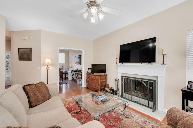 living room featuring a fireplace with raised hearth, a ceiling fan, and wood finished floors