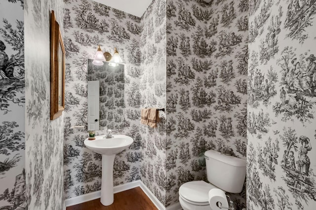 bathroom with wallpapered walls, toilet, wood finished floors, and baseboards