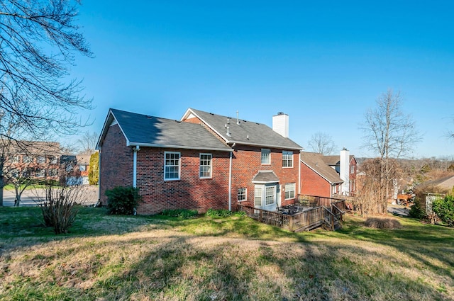 back of property with brick siding, a wooden deck, a chimney, and a yard