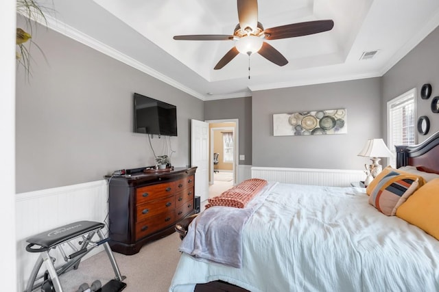 carpeted bedroom with a wainscoted wall, a tray ceiling, and ceiling fan
