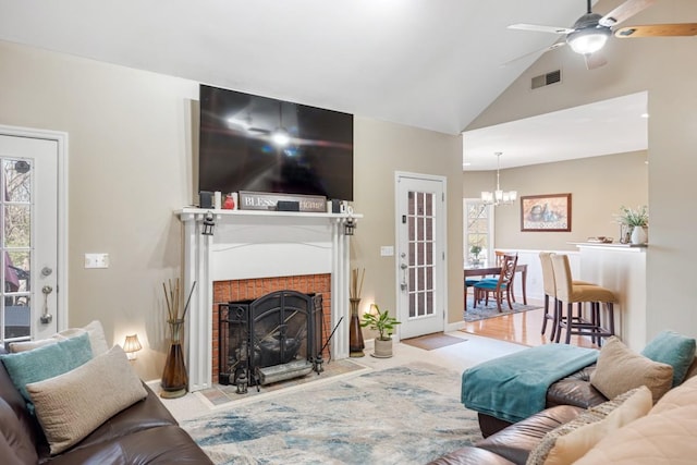 living area featuring high vaulted ceiling, ceiling fan with notable chandelier, a fireplace, and visible vents