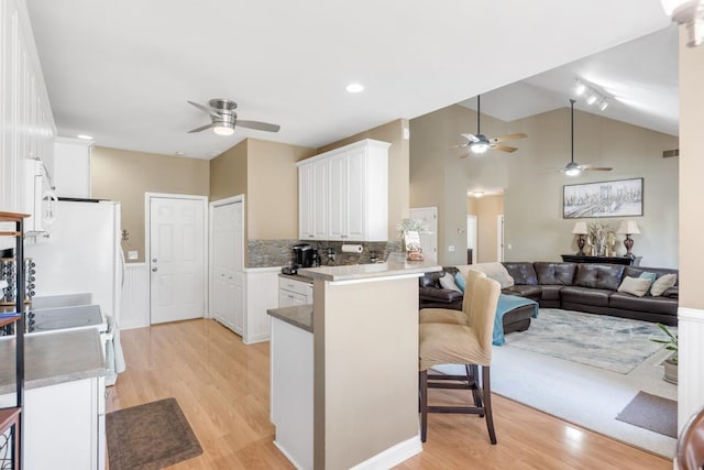 kitchen with a ceiling fan, light wood-style flooring, a breakfast bar, white cabinets, and a peninsula