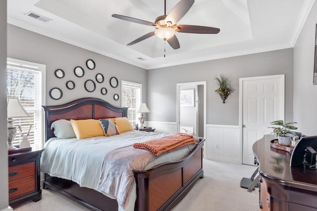 bedroom with crown molding, a raised ceiling, visible vents, light carpet, and wainscoting