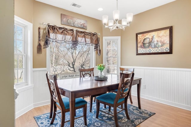 dining area featuring visible vents, light wood-style floors, a notable chandelier, and wainscoting