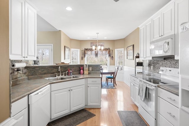 kitchen with a wainscoted wall, a peninsula, white appliances, a sink, and an inviting chandelier