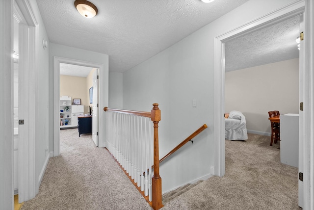 hallway with carpet flooring, an upstairs landing, baseboards, and a textured ceiling