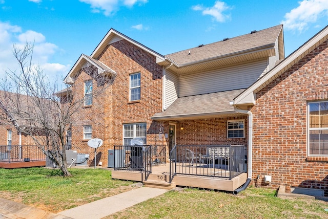 traditional-style home with brick siding, a deck, a front lawn, and roof with shingles