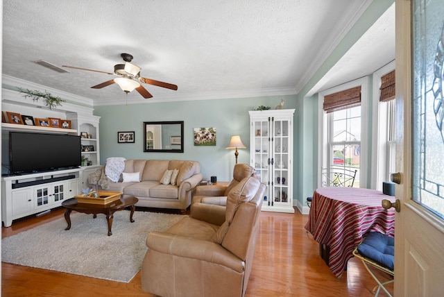 living room featuring wood finished floors, visible vents, ceiling fan, a textured ceiling, and crown molding