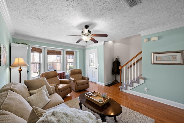 living room with visible vents, wood finished floors, crown molding, and stairway