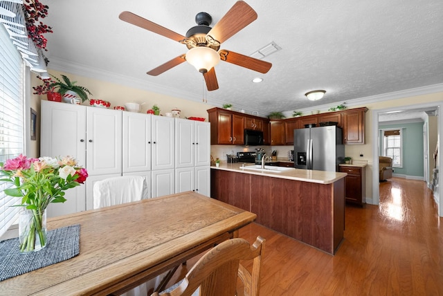 kitchen featuring black microwave, ornamental molding, stainless steel fridge with ice dispenser, and light countertops