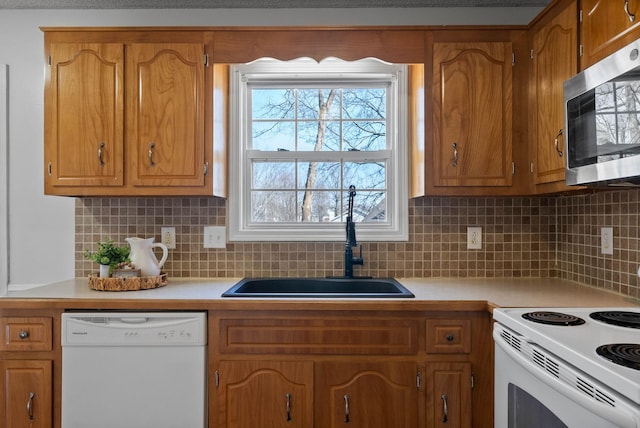 kitchen featuring light countertops, decorative backsplash, brown cabinetry, white appliances, and a sink