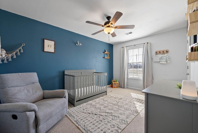 carpeted bedroom with visible vents, a nursery area, a ceiling fan, and baseboards