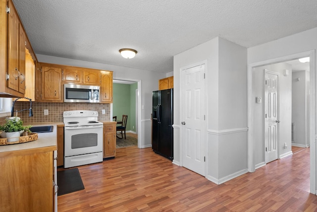 kitchen featuring white electric range oven, a sink, light countertops, stainless steel microwave, and black fridge