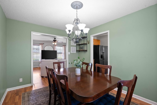 dining area with ceiling fan with notable chandelier, wood finished floors, baseboards, and a textured ceiling